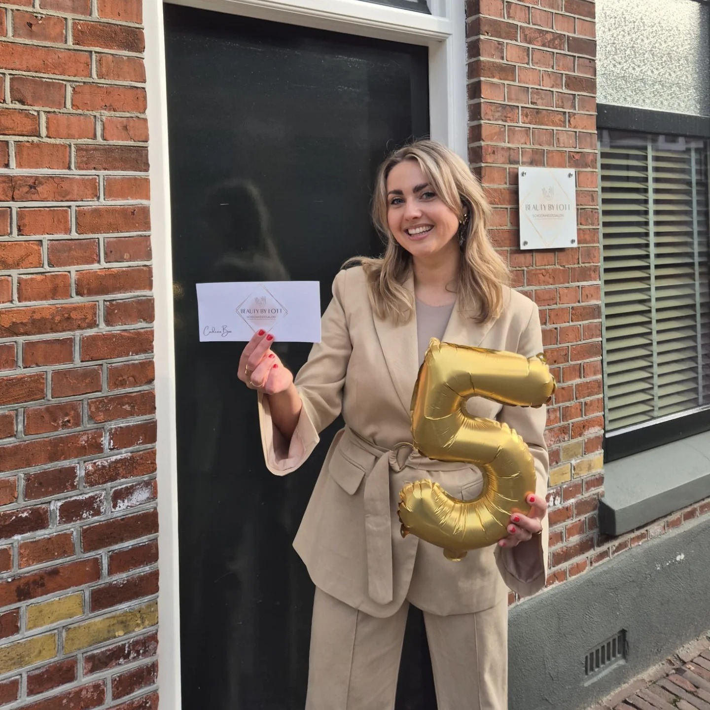 Annelot bij de deur van haar salon met een gouden ballon in de vorm van een 5